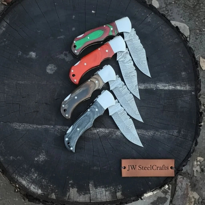 folding knives with red, green, black, and brown handles, patterned steel blades, and polished silver bolsters.