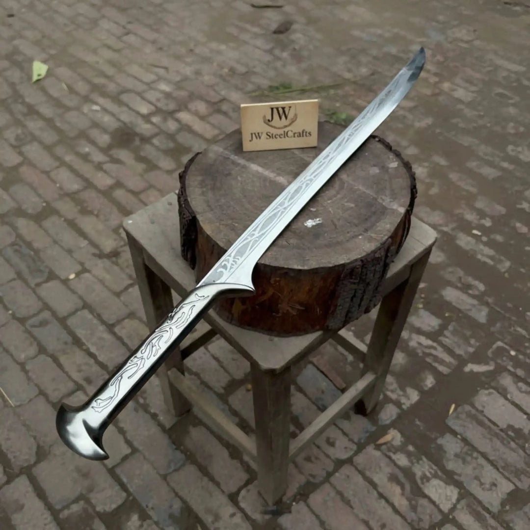 Top-down view of an ornate fantasy elven sword with full-length floral and scrollwork etchings and a curved hooked pommel, on a rustic wood log stool outdoors.