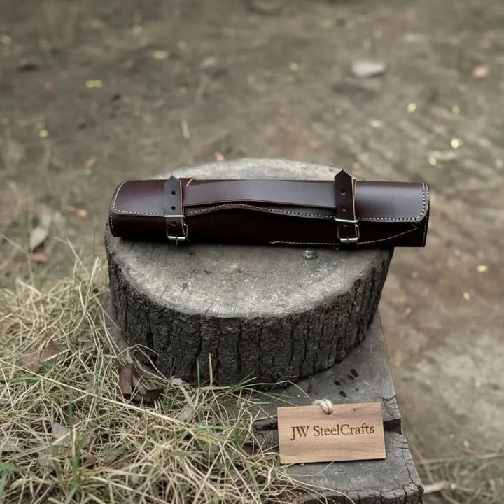 Portable genuine leather chef knife storage roll in dark espresso brown with double belt buckle straps resting on a wooden stump in natural light
