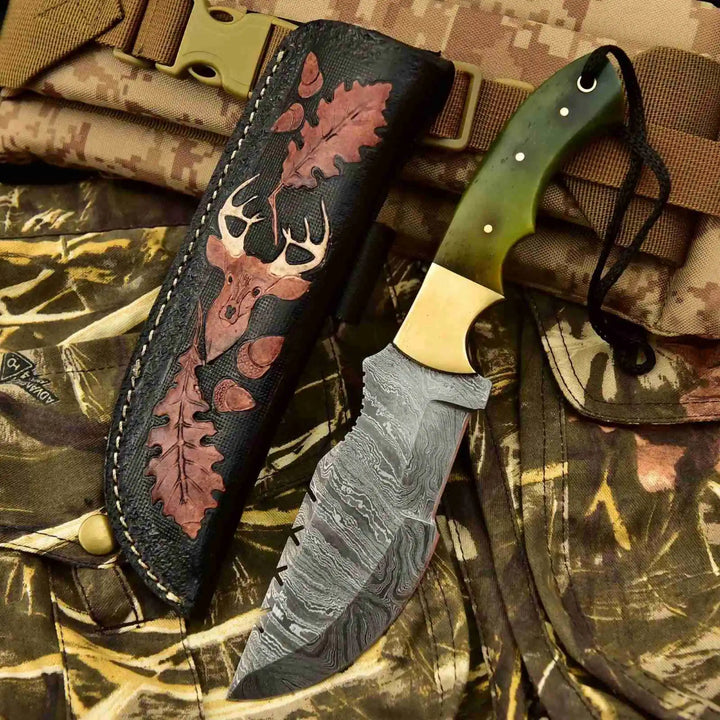 Damascus skinner knives with green, ivory, and brown handles displayed between decorative leather sheaths on camouflage fabric.