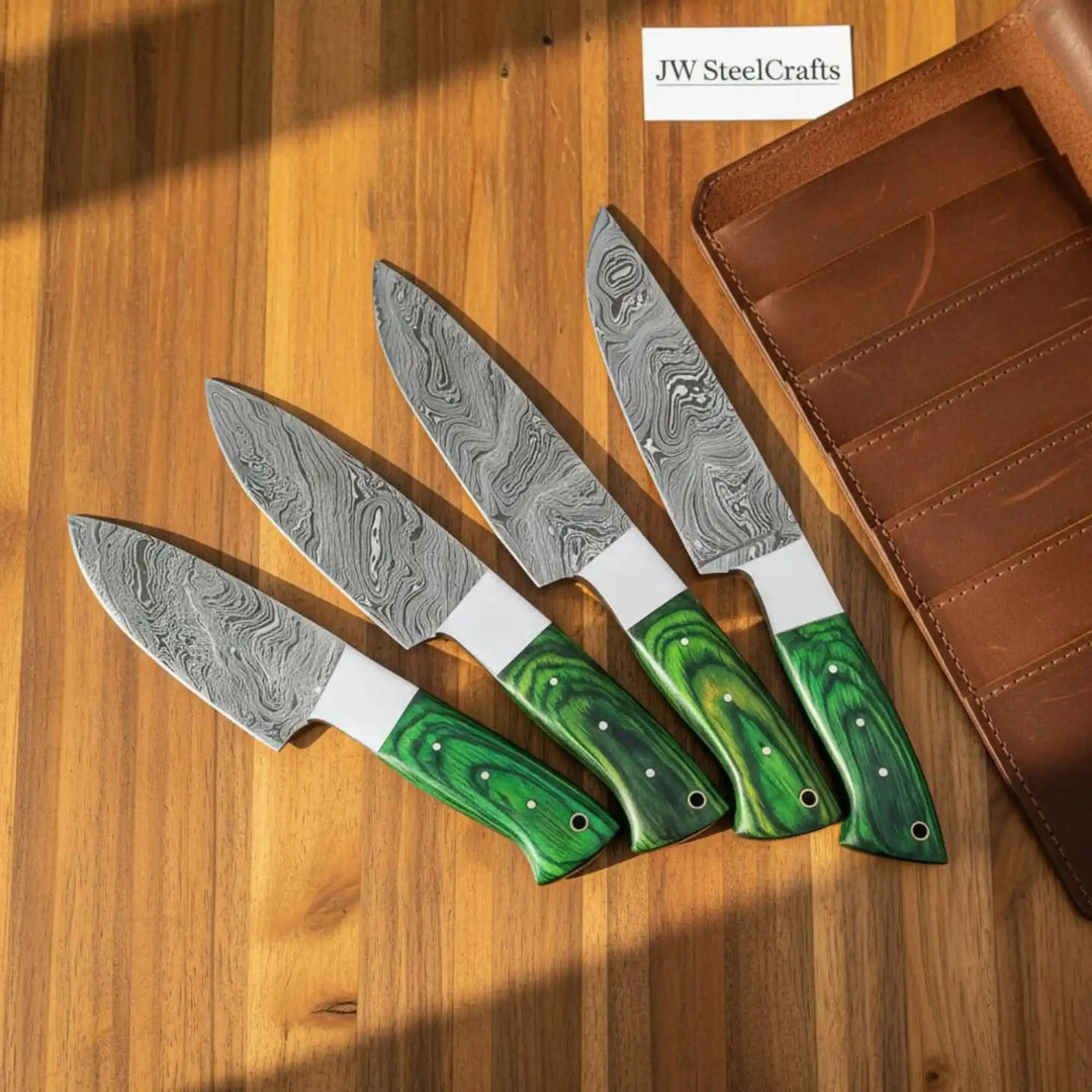 Four Damascus kitchen knives with green wood handles displayed on a wooden surface