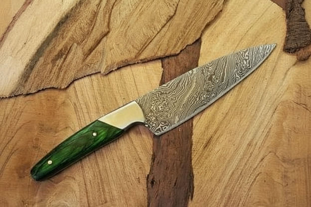 Handmade Damascus steel chef knife with a patterned blade and green resin handle displayed on a natural wood surface.