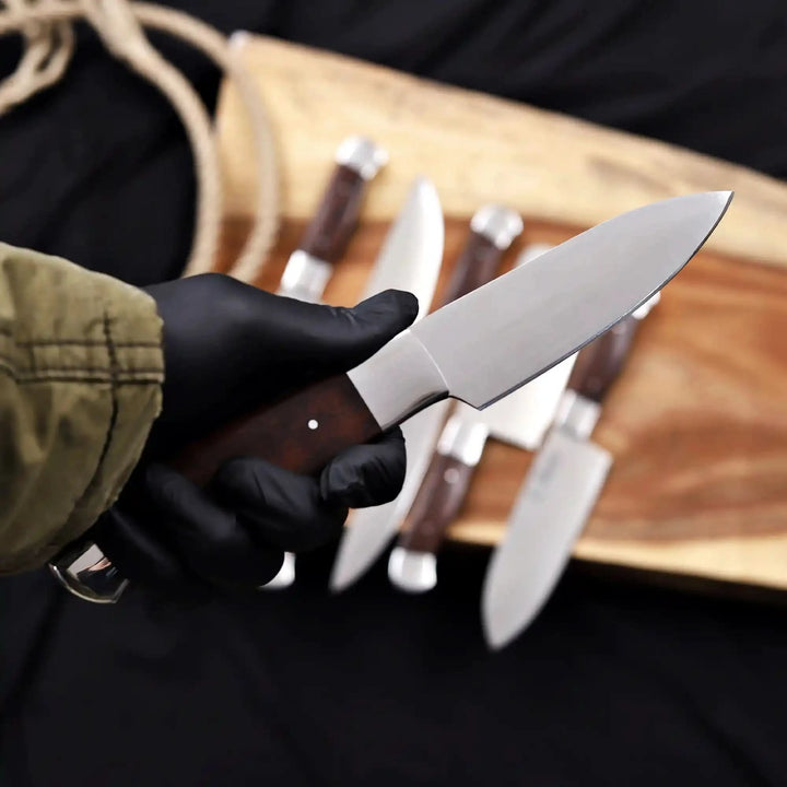 Close-up of a full tang kitchen knife being held by a person in black gloves, showcasing the balanced weight and ergonomic design.