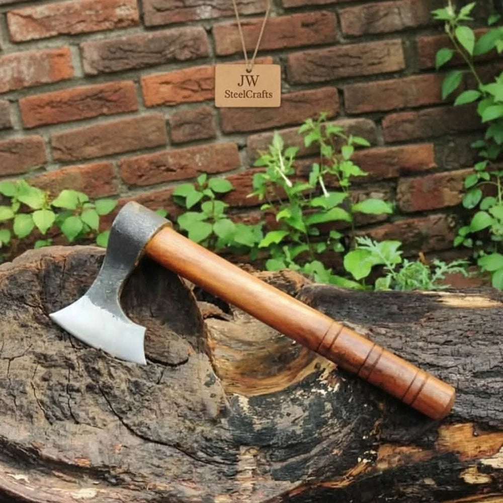     Artisan-crafted camping hatchet featuring a forged steel head and polished wooden grip displayed near a rustic brick wall.