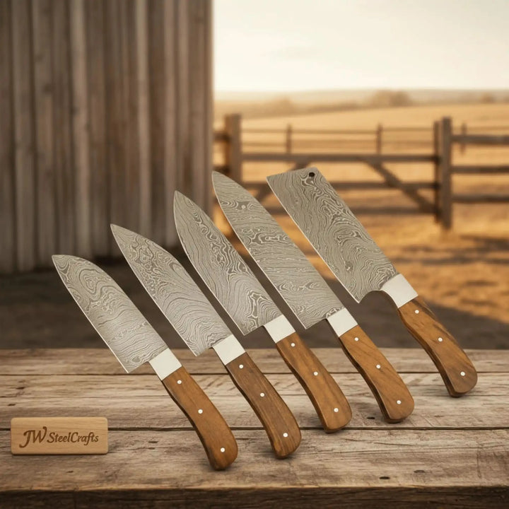 Four Damascus kitchen knives standing upright on rustic wooden table in countryside setting.