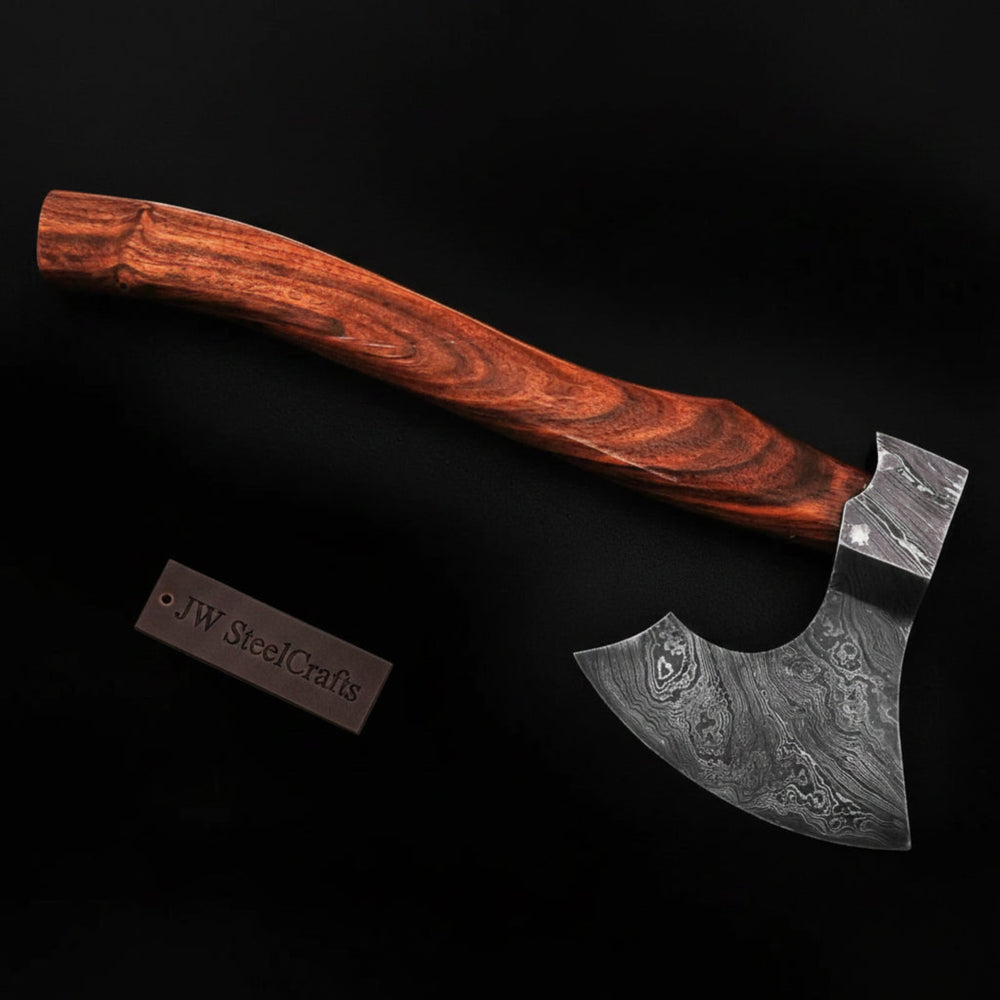 Premium camping axe with a natural wood handle, patterned steel blade, and leather protective cover displayed outdoors.