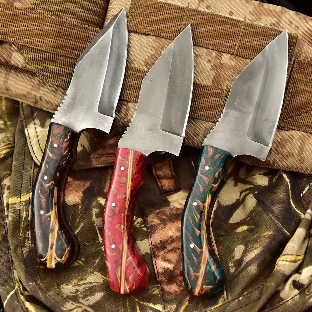 Three handmade custom push daggers with polished steel blades and colorful resin handles displayed on camouflage fabric.