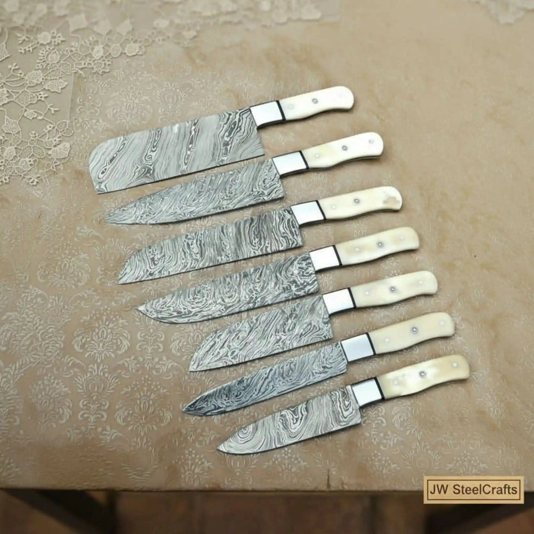 Ivory handle Damascus chef knives displayed on decorative textured background.