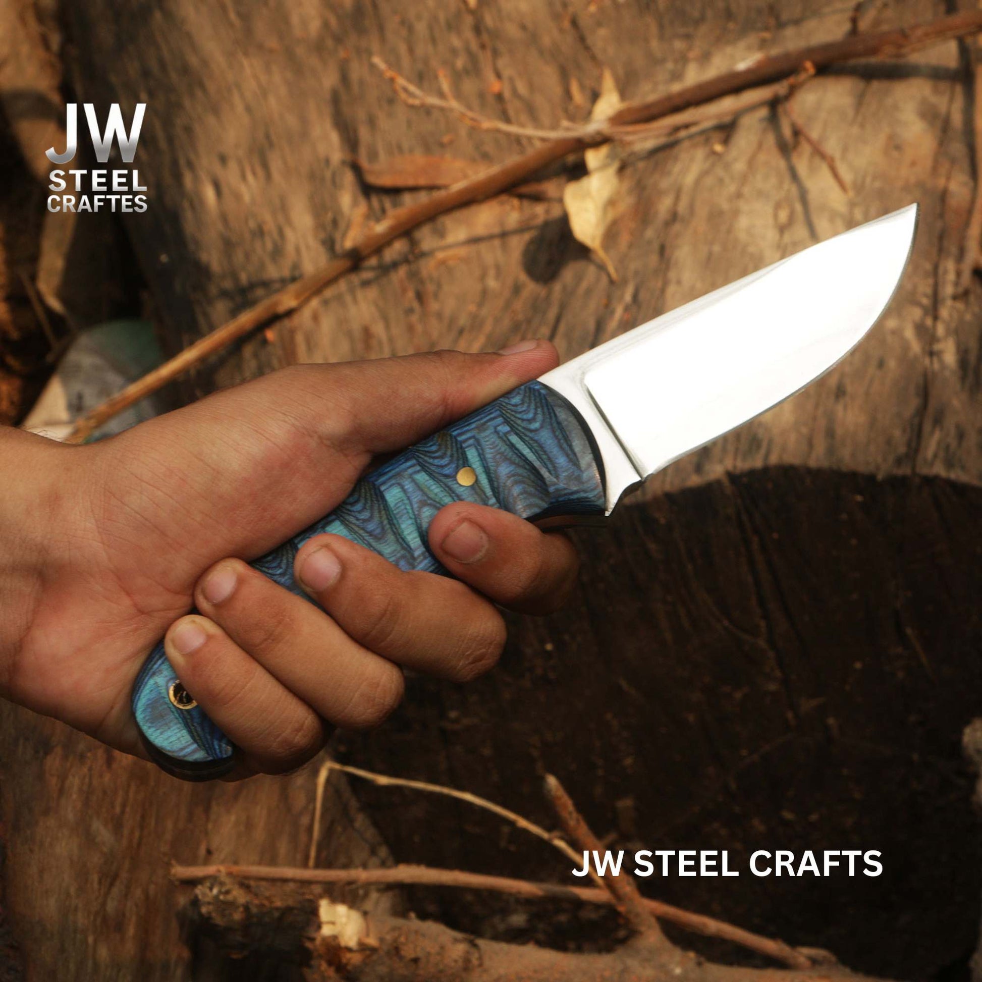 Hand holding a knife with a blue handle against a wooden background, branded 'JW Steel Crafts'.