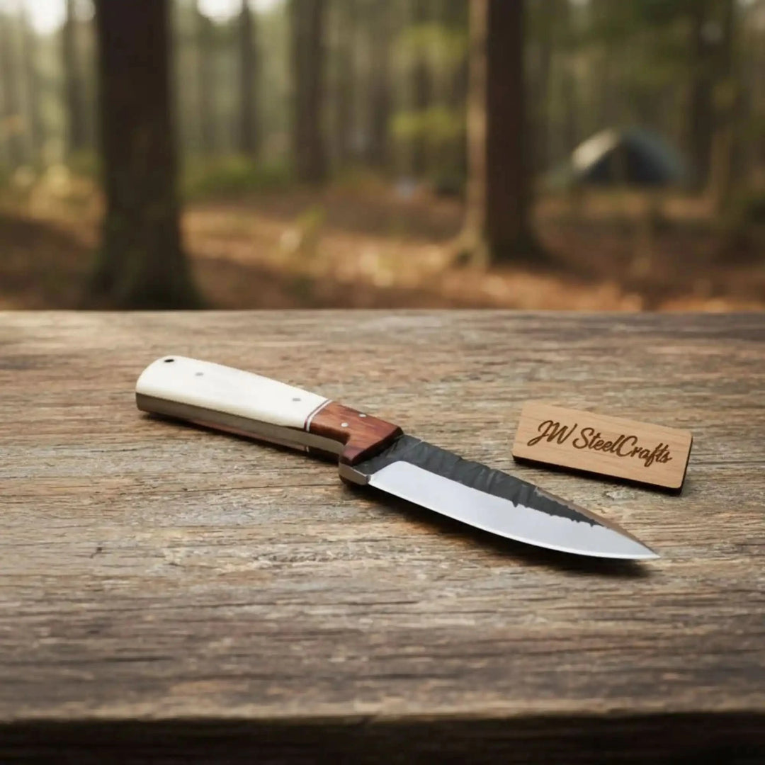 Compact hunting knife with bone handle, brown wood bolster section, polished steel edge, and forest camp table display.