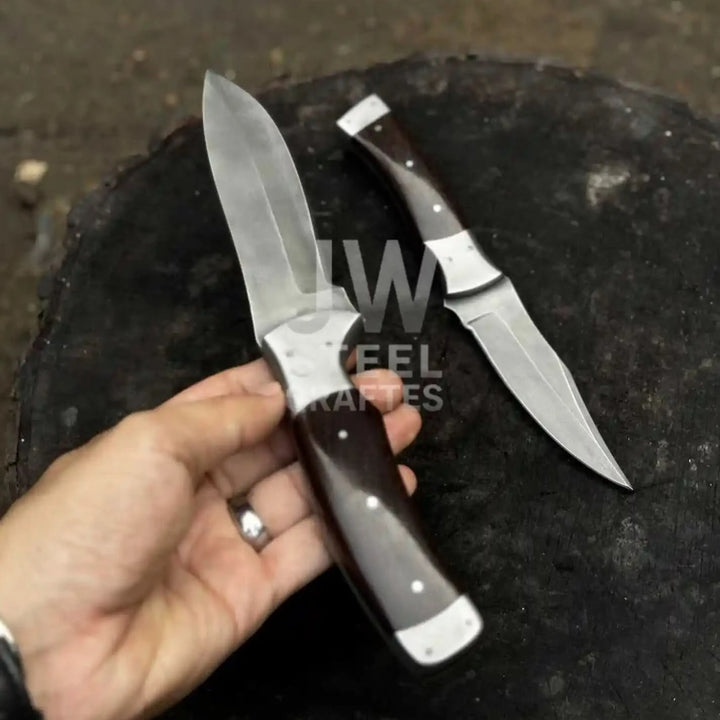 Hand holding handmade hunting knife with dark rosewood handle and polished steel blade