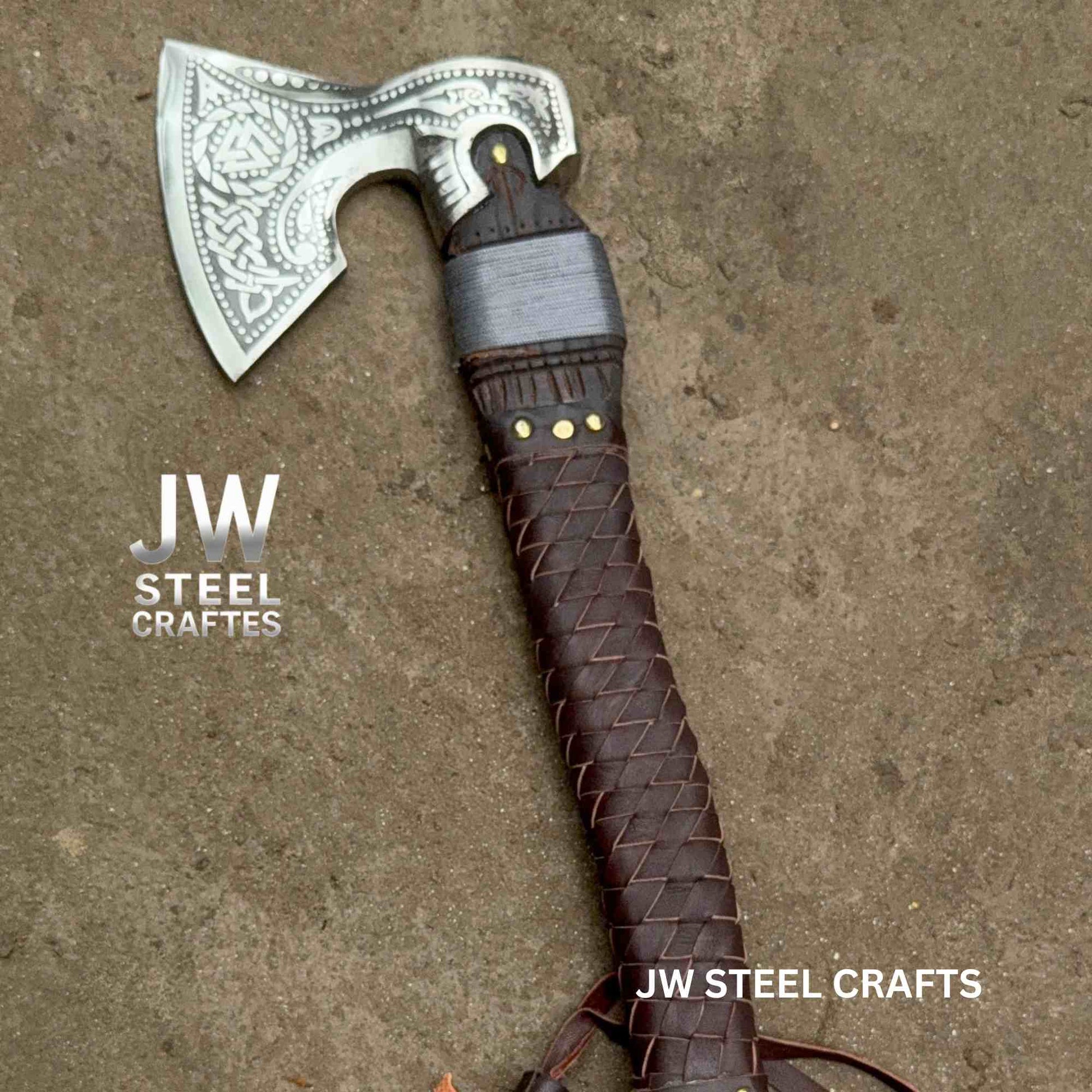 Decorative axe with braided brown handle on a textured surface, branded 'JW Steel Crafts'.