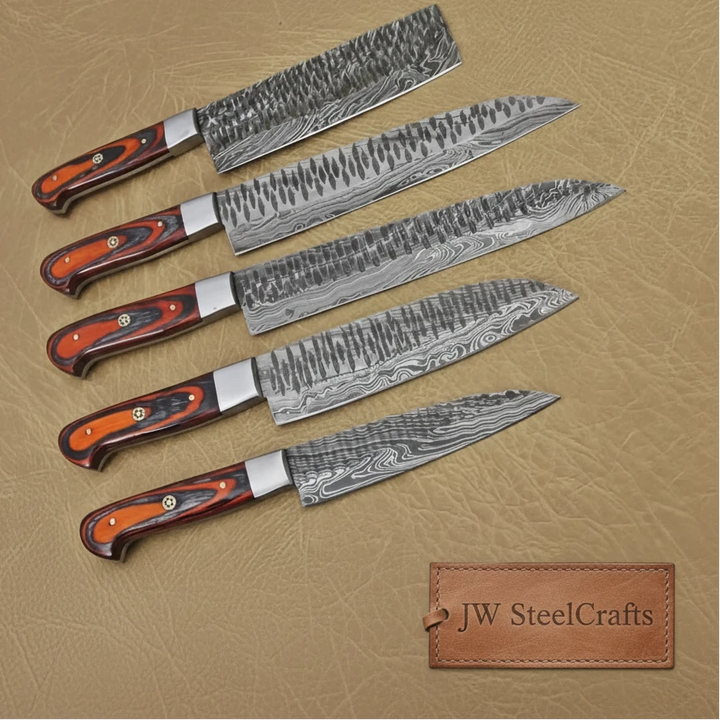 Five high carbon Damascus steel kitchen knives with orange and black ergonomic handles displayed diagonally on textured beige background.