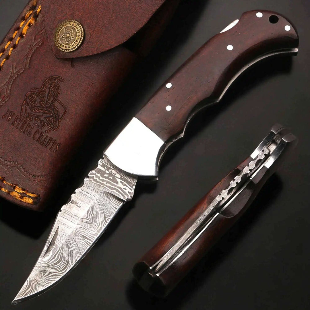     Wildbranch Damascus folding knife with darkwood scales and sharp patterned steel blade on black surface