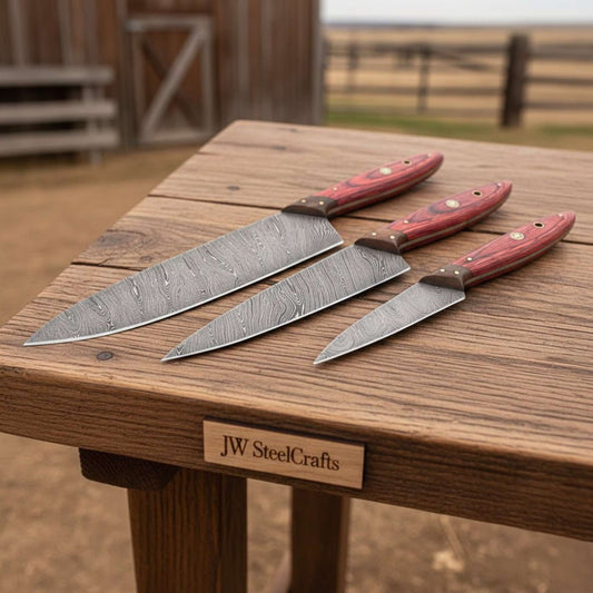 JW SteelCrafts handmade Damascus kitchen knife set with red wood handles on wooden table.