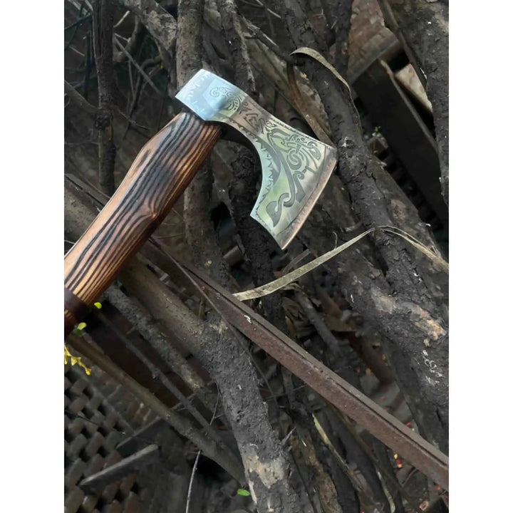 Legacy-inspired Nordic hand axe showcasing polished engraved steel and dark wood craftsmanship outdoors.
