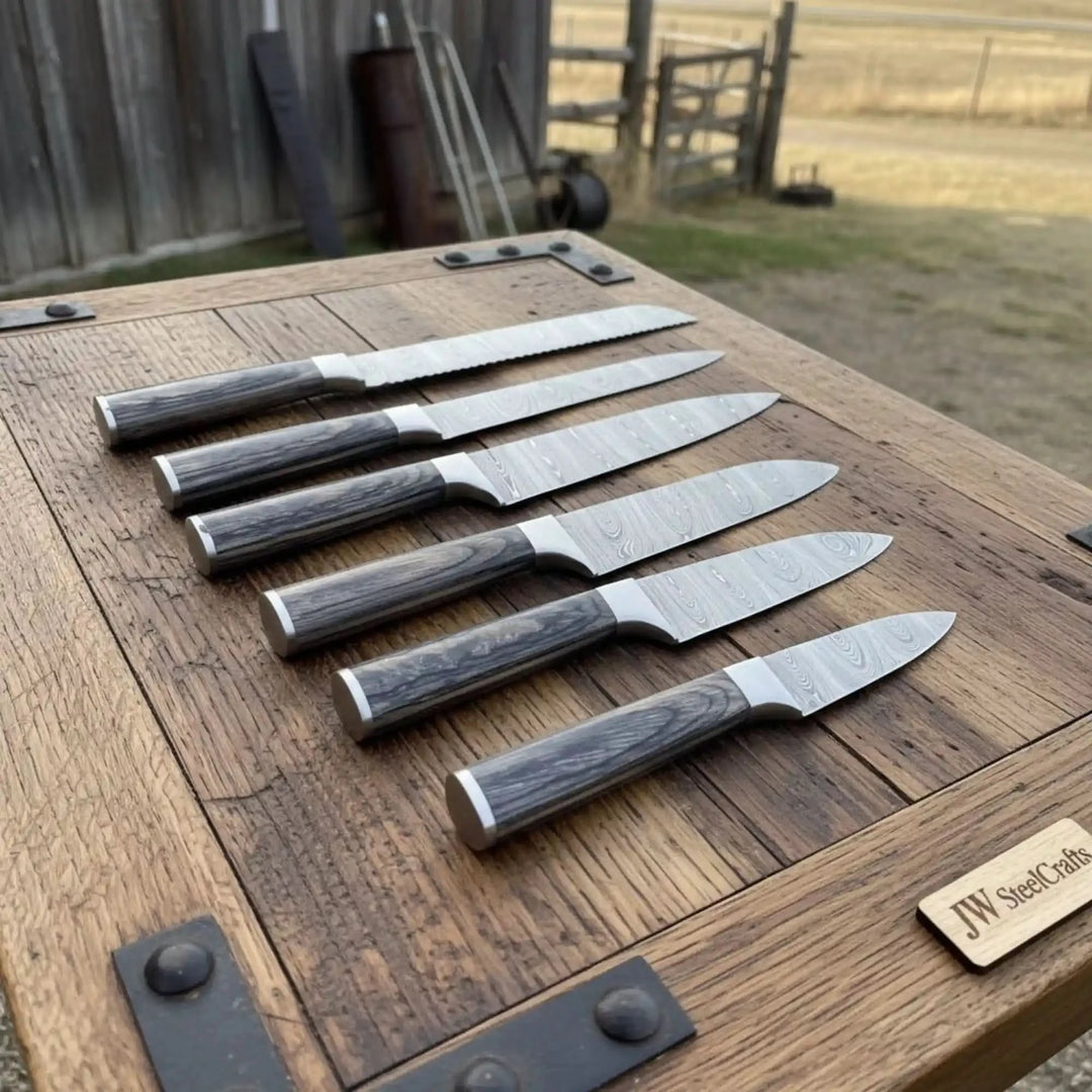 Polished chef knives arranged diagonally across rugged tabletop with decorative Damascus steel detailing.