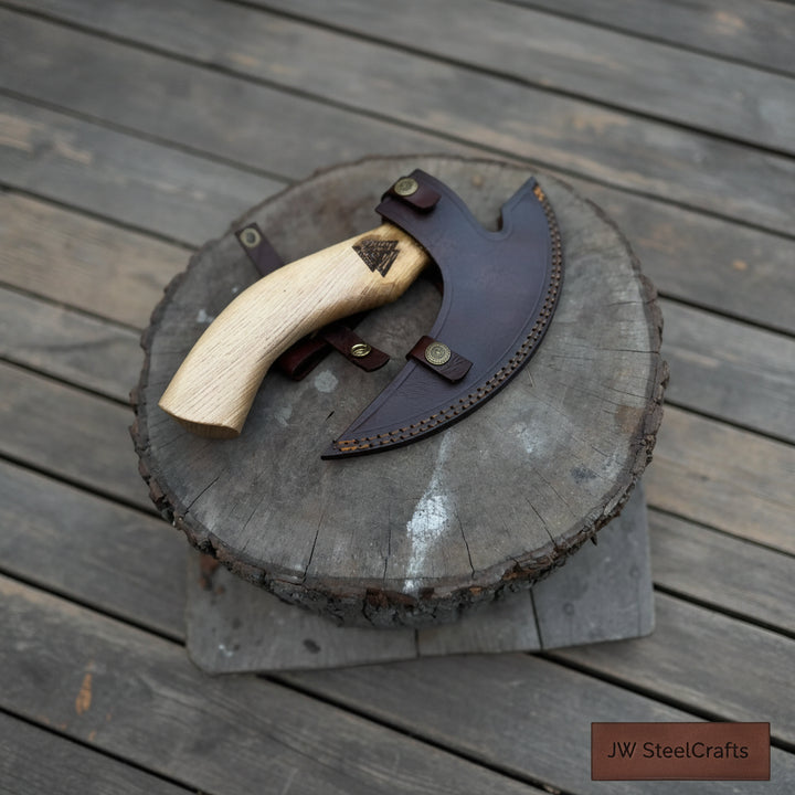 Premium engraved camping hatchet displayed on a wooden stump with leather sheath and forest background.