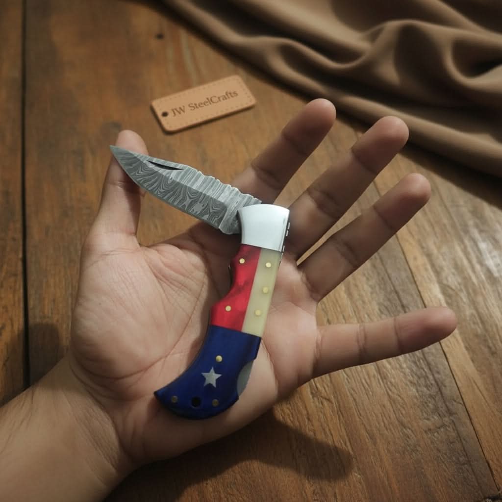     Bluevalley Damascus folding knife with patriotic handle and textured steel blade held over wooden surface