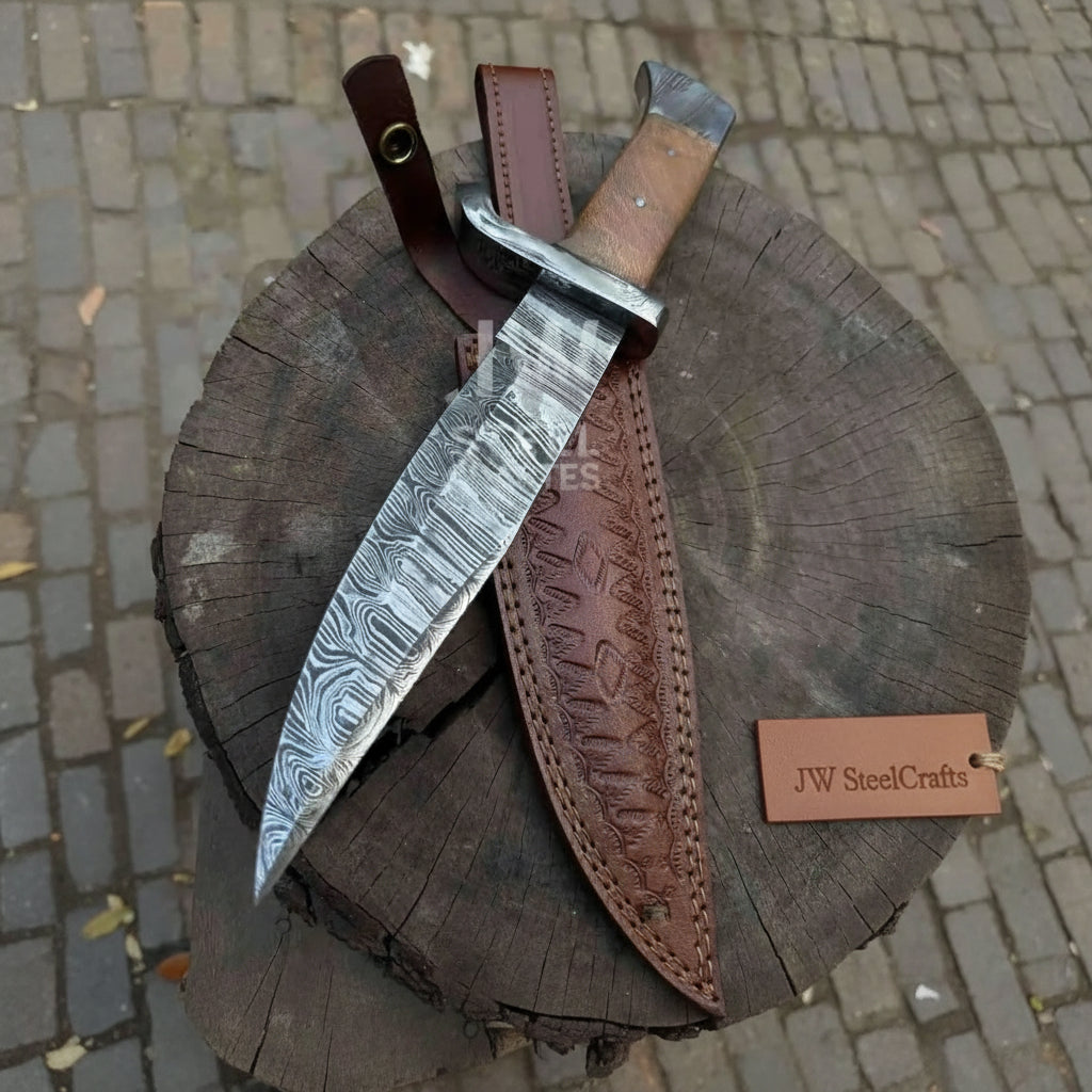 Forged Damascus hunting blade with polished guard, wood handle, tooled leather sheath, and round stump product setup.