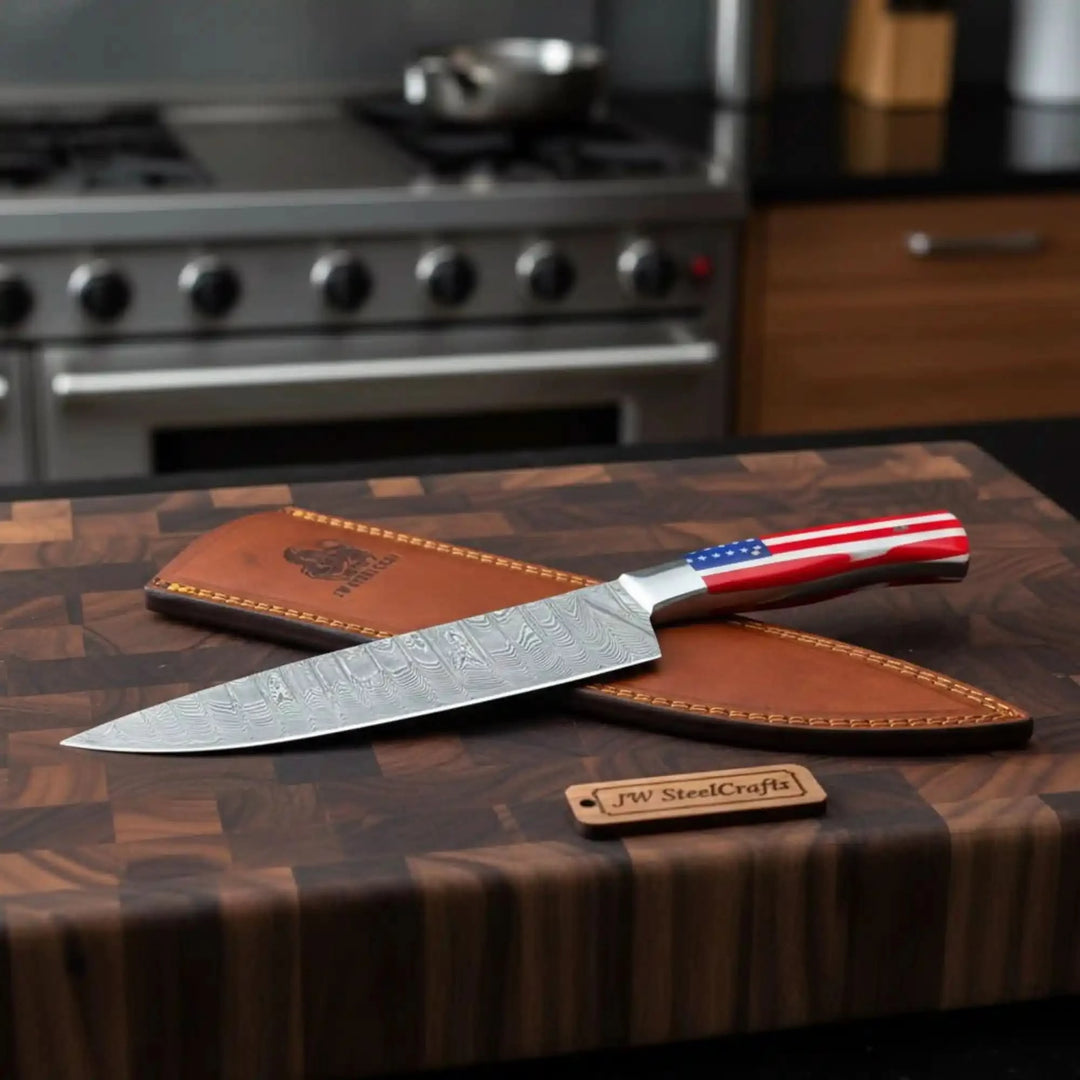 Culinary Damascus knife with American flag grip, long patterned blade, polished bolster, and kitchen counter background.