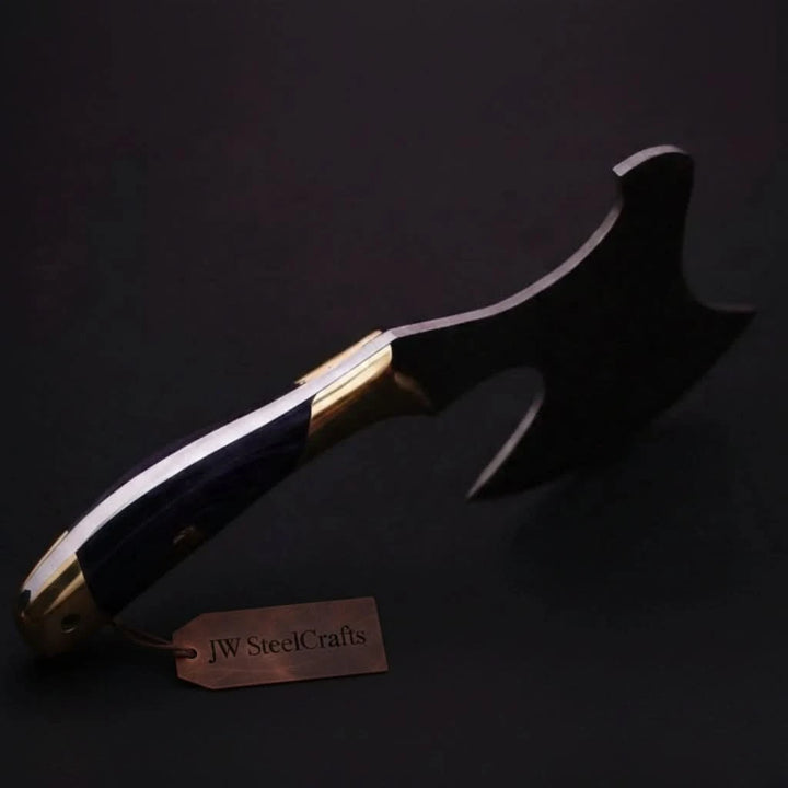 Artisan forged Damascus camp cleaver knife with a curved blue resin handle and leather carrying sheath displayed in a rustic environment.