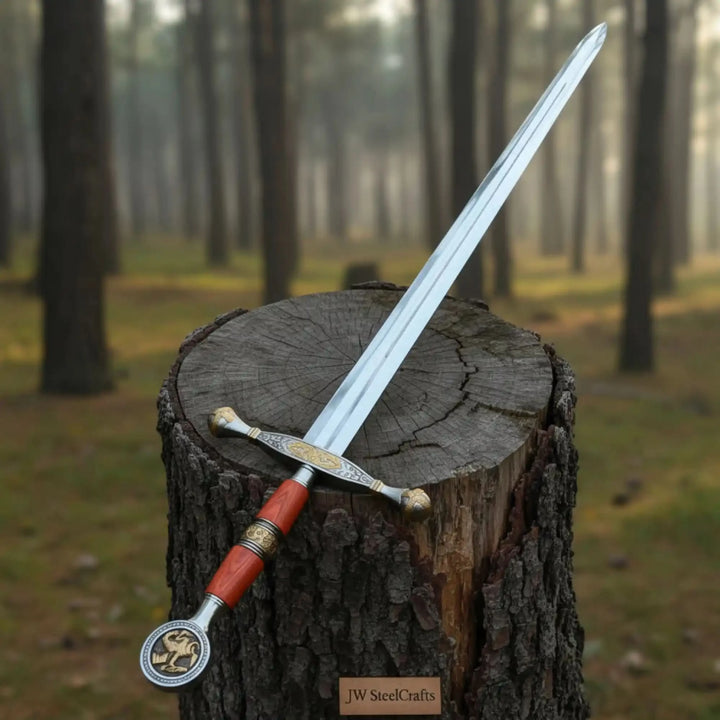 A decorative medieval sword with a red grip and gold crossguard resting on a weathered tree stump in a misty pine forest