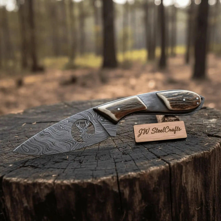 Hunting skinner Damascus knife with stag style handle, decorative deer cutout, and brown leather sheath on wooden table.