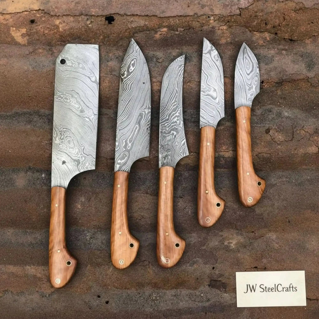 Handcrafted Damascus steel knife collection featuring cleaver and four chef knives with matching warm olive wood grips and white pin handles laid flat on a weathered brick surface
