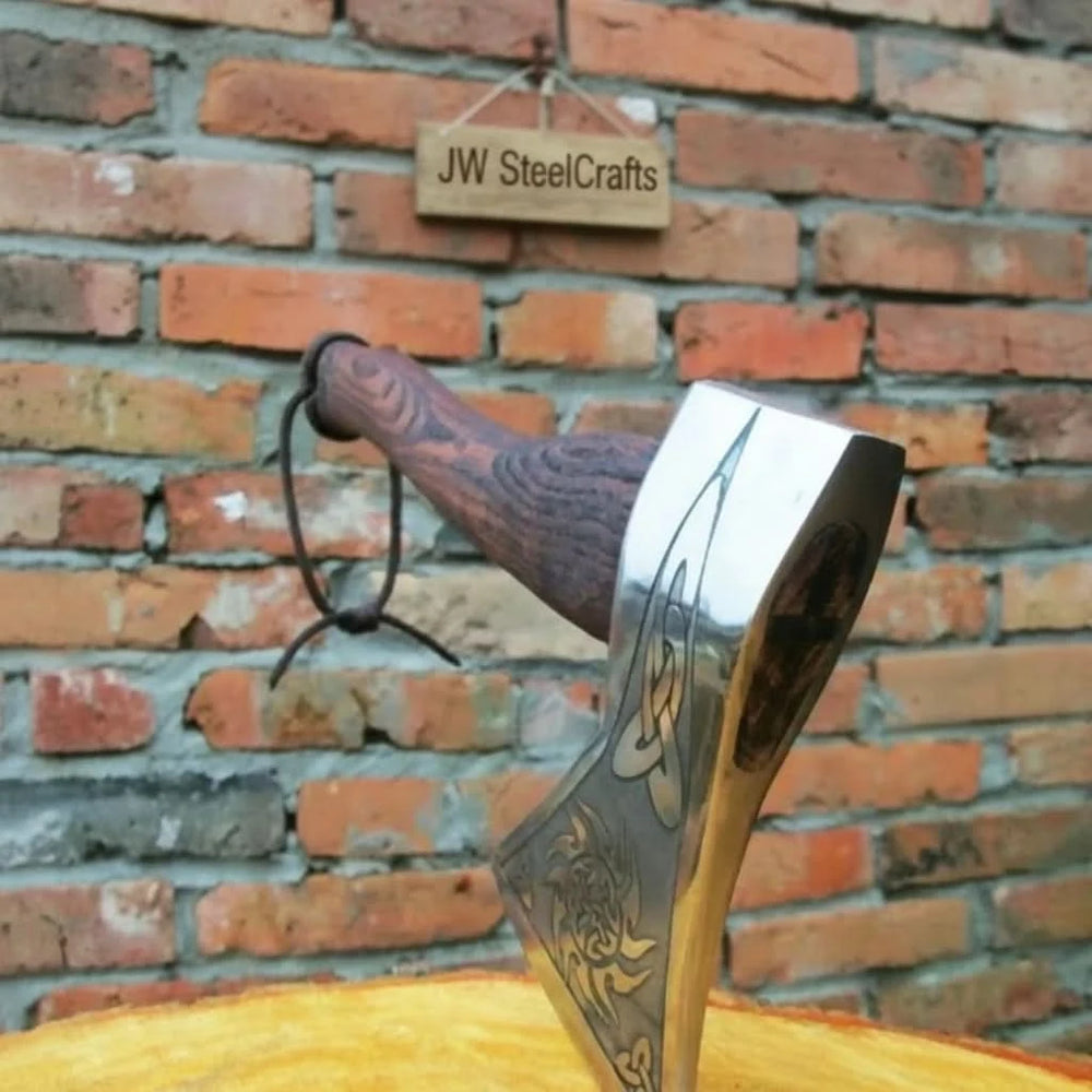     Handmade Viking-style axe with Celtic knot engravings and polished wooden handle displayed on a weathered outdoor wooden table.