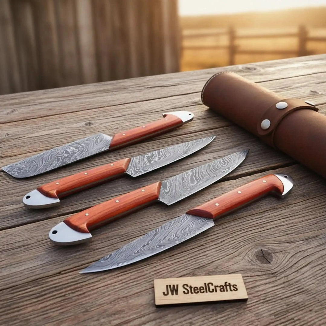 Four handmade Damascus outdoor hunting knives with vibrant orange rosewood handles and polished silver bolsters fanned on a weathered ranch wood table with rolled leather carrying case and warm golden background
