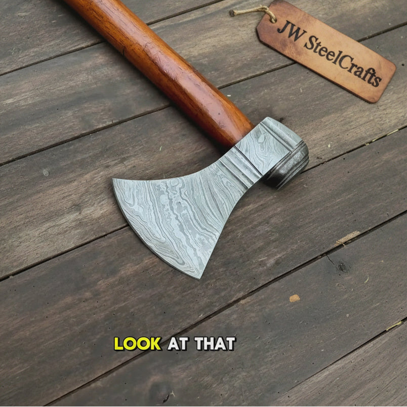 Powerful Damascus bearded hatchet with broad curved blade and rich wooden handle resting on timber.