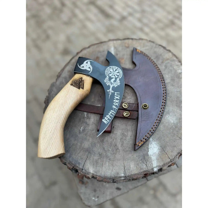 Handcrafted crescent blade hatchet with ergonomic wooden handle and leather cover photographed outdoors.