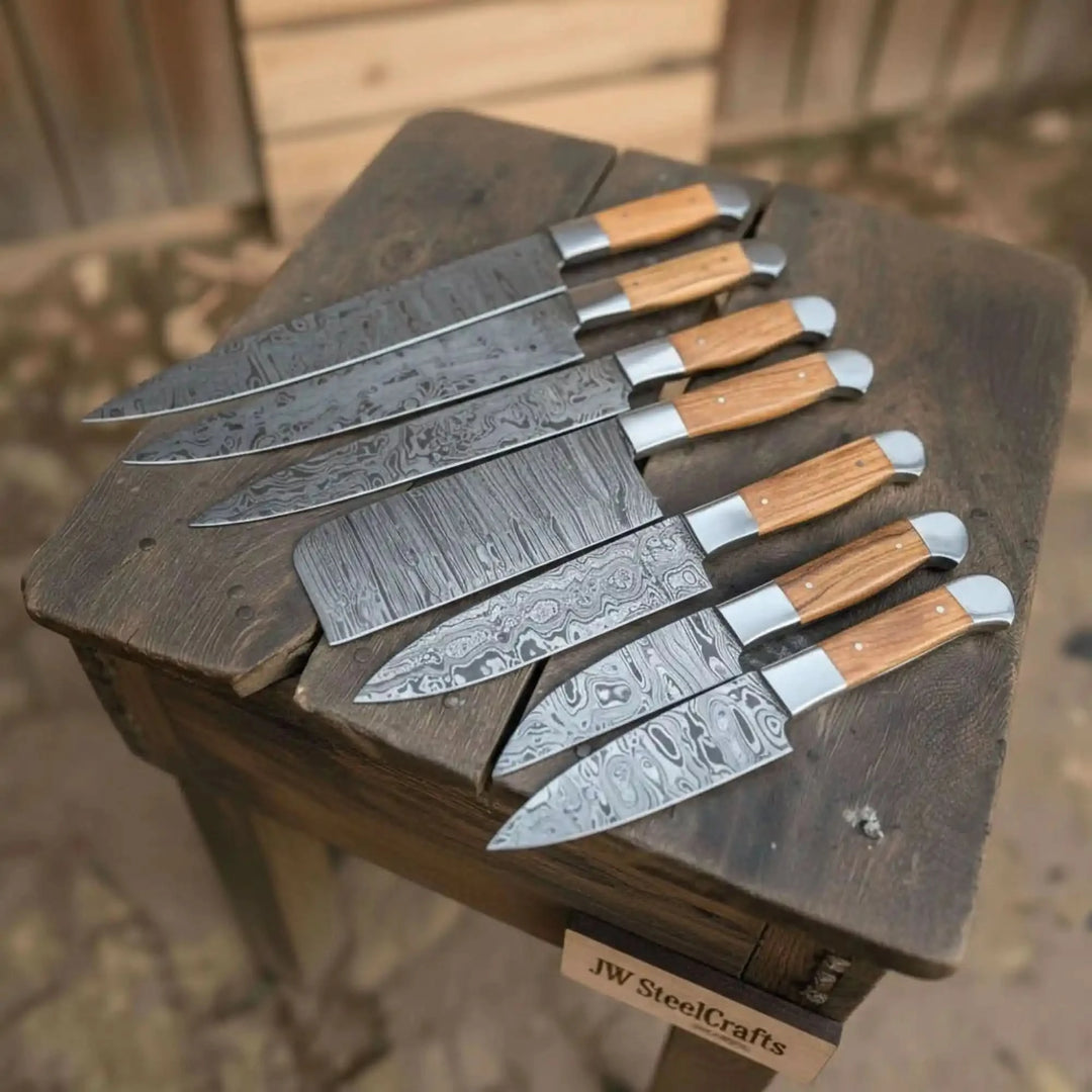Wood handle Damascus chef knife assortment displayed in rustic outdoor environment