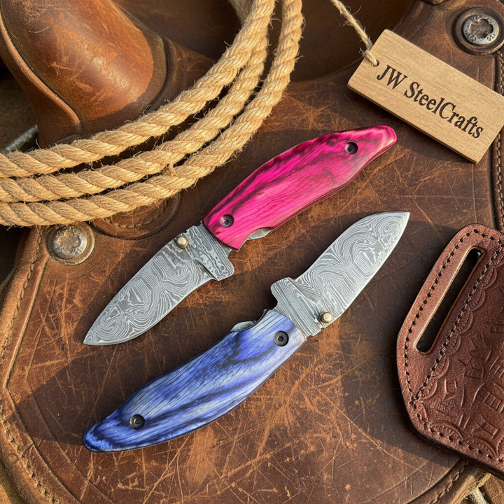 Pakka Wood Handmade Damascus Steel Skinner Knife Two Knives With Pink And Blue Handles On A Rustic Leather Surface