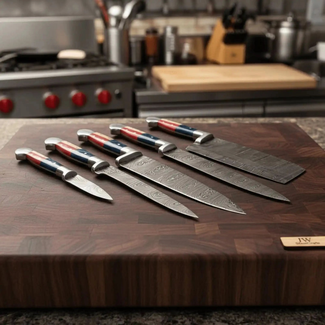 Dramatic kitchen atmosphere shot of five handforged Damascus chef knives with patriotic Texas flag red blue white handles fanned on a thick end-grain walnut board with stove visible in background
