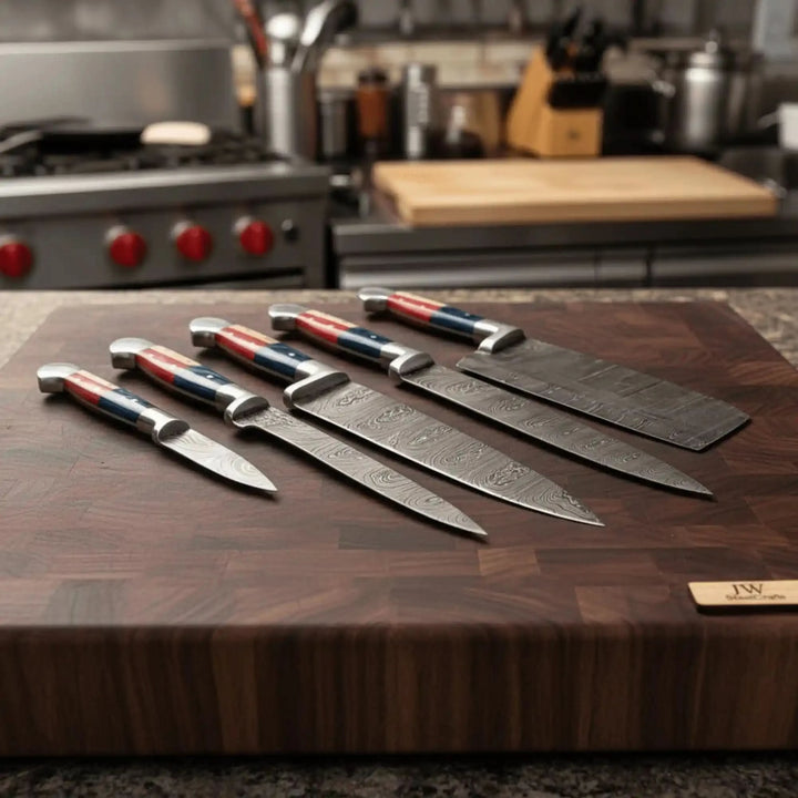Dramatic kitchen atmosphere shot of five handforged Damascus chef knives with patriotic Texas flag red blue white handles fanned on a thick end-grain walnut board with stove visible in background
