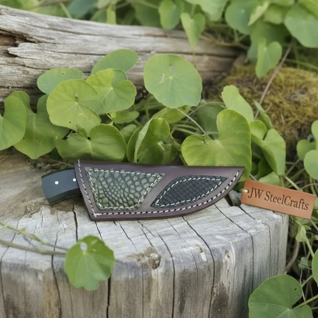 Custom outdoor knife with curved Damascus blade, black handle, leather sheath, and forest tree stump setting