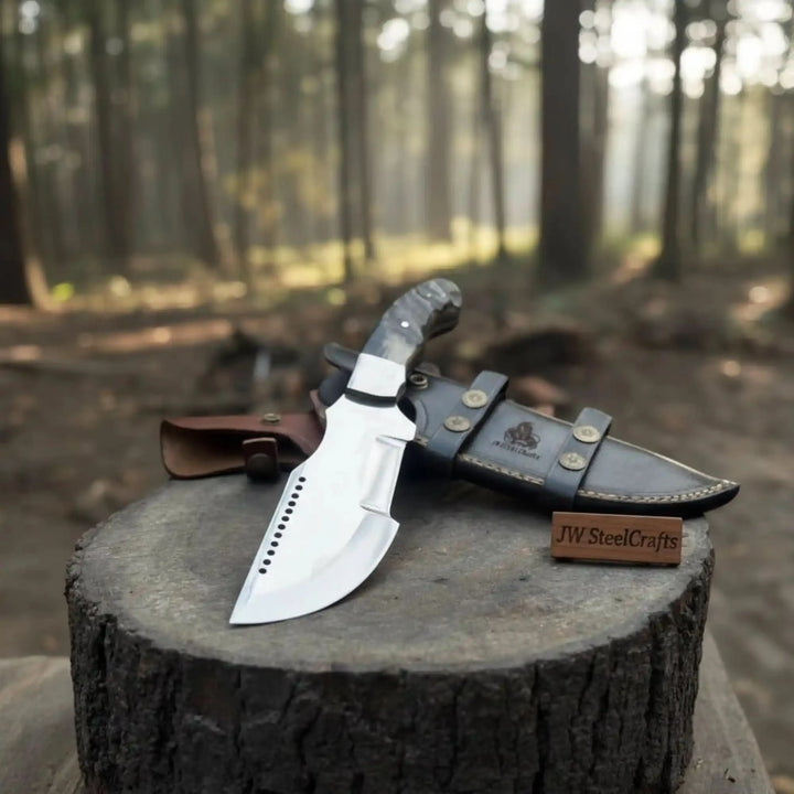 Outdoor fixed blade knife displayed with dual leather sheaths, one brown and one black, on a round tree stump.