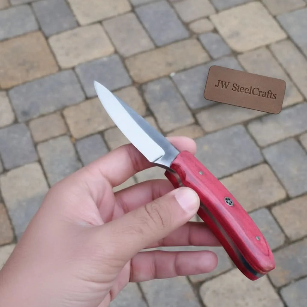 Compact hunting knife with red handle, polished steel blade, decorative mosaic pin, and forest product photography.