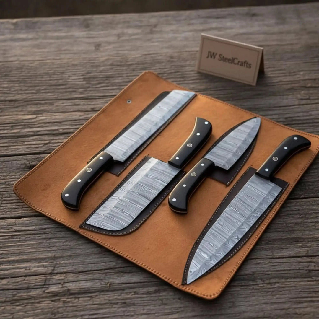 Flat lay of four handforged Damascus kitchen knives with riveted black ebony grips displayed in individual slots of an unrolled caramel leather knife case on a wood surface
