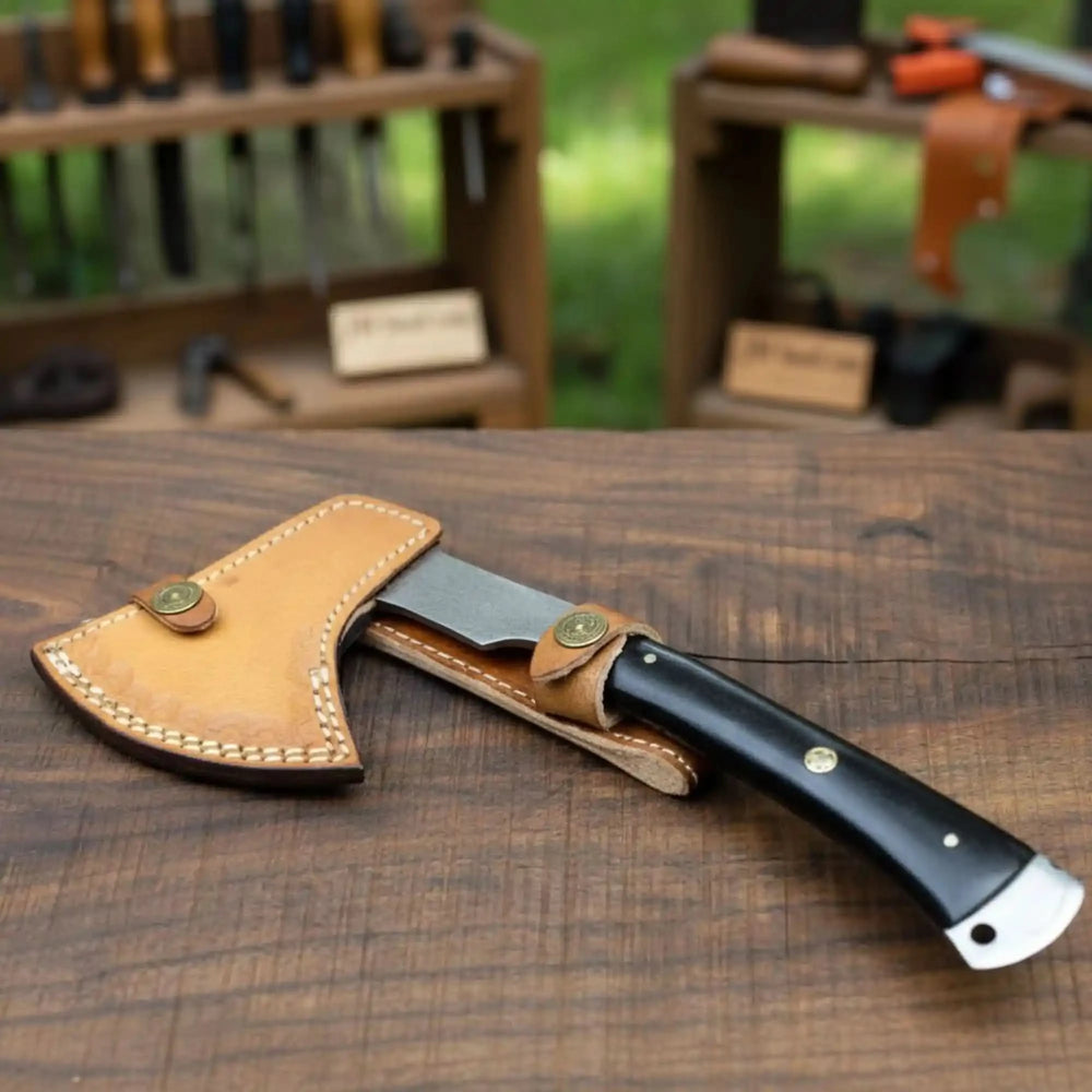 Artisan forged Damascus axe with detailed steel patterns and a smooth black grip handle photographed on a rustic wood background outdoors.