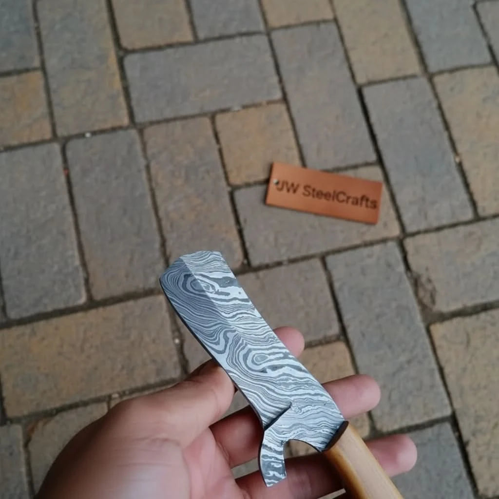 Forged Damascus cleaver knife with wood grip, dark patterned steel, hook-style heel, and woodland table setting.