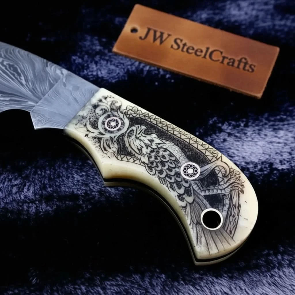 Custom skinning knife with Damascus blade, engraved grip, decorative pins, and black lanyard hole on handle end.