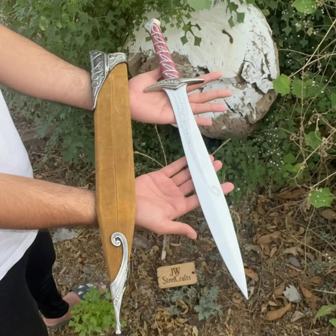 An elvish-inspired short sword and wooden scabbard set, featuring a polished engraved blade, vivid red grip, and ornate silver crossguard on a natural tree stump.