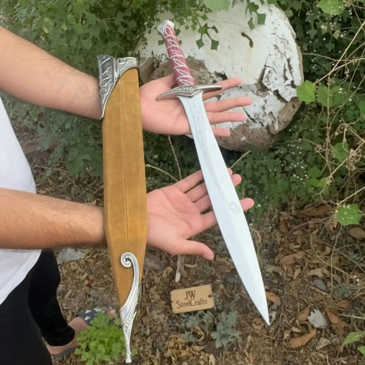 An elvish-inspired short sword and wooden scabbard set, featuring a polished engraved blade, vivid red grip, and ornate silver crossguard on a natural tree stump.