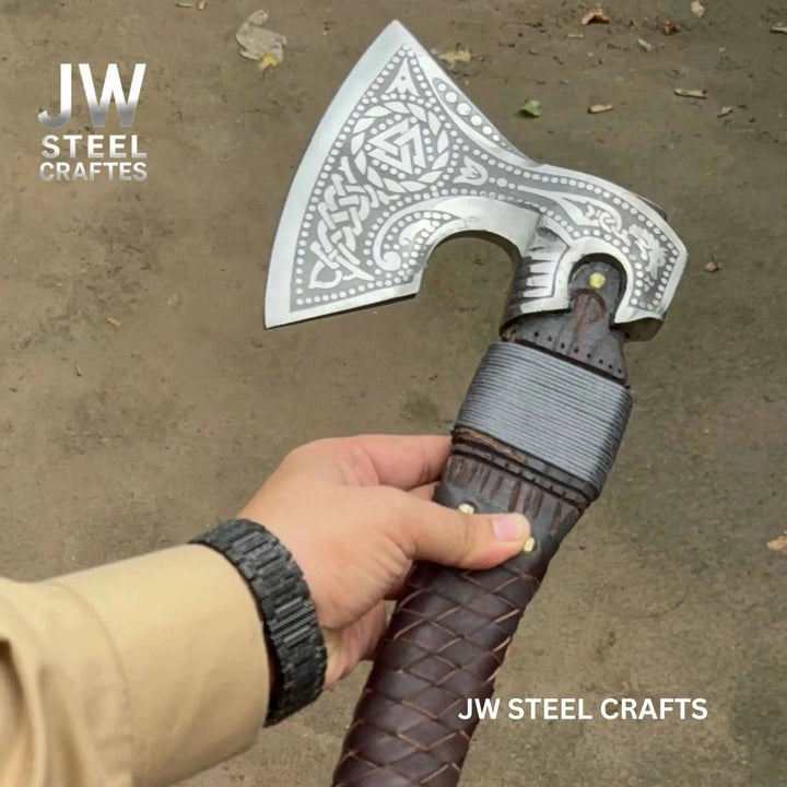 Decorative Viking battle hatchet with artistic Celtic engravings and handcrafted leather handle outdoors.