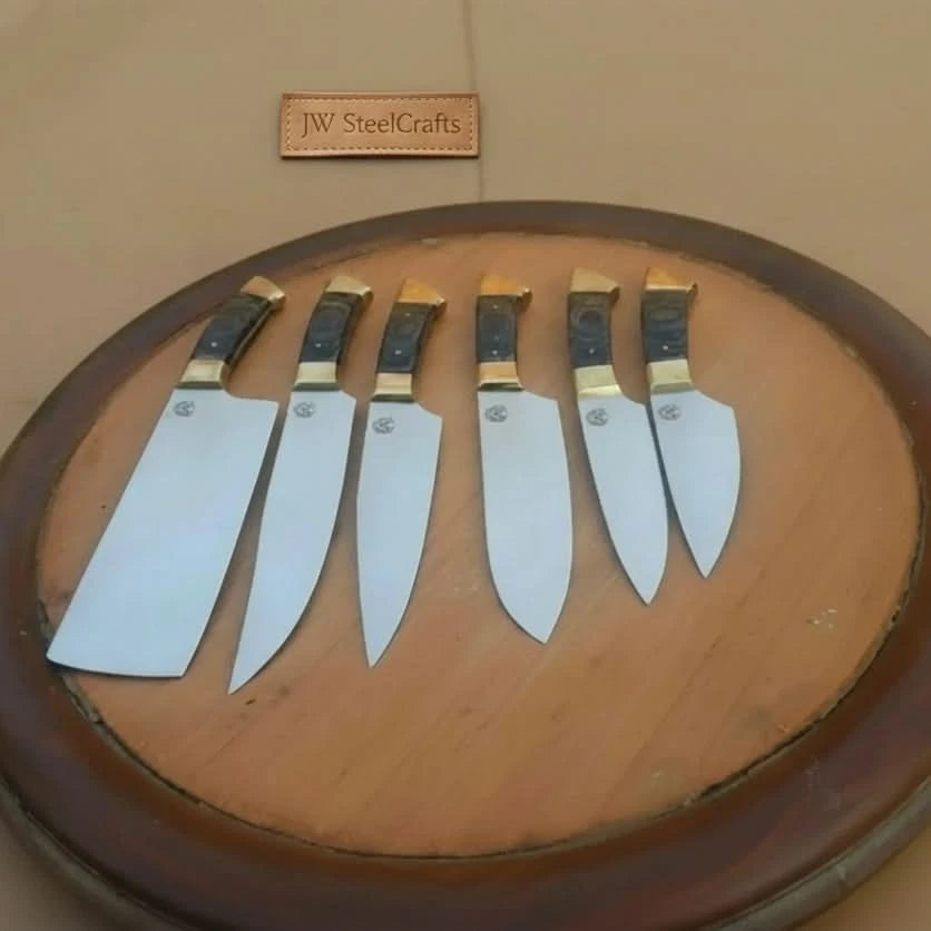 Multiple knife sizes are displayed together on a circular wooden tabletop for a clean presentation.