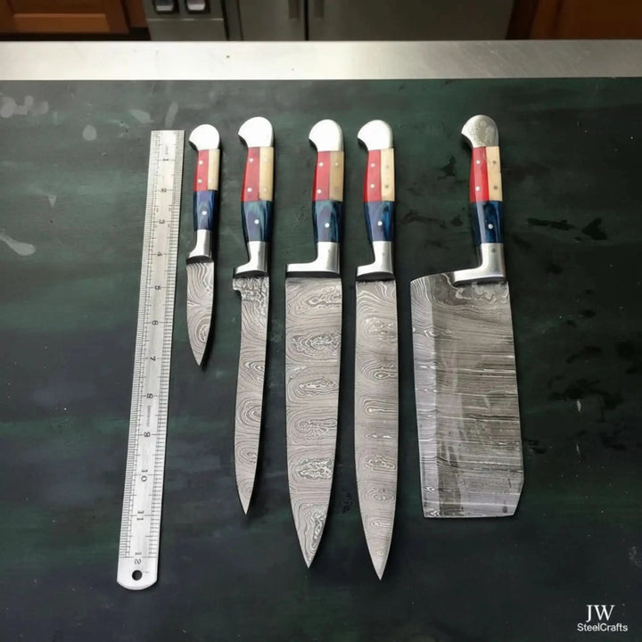 Size comparison overhead shot of JW SteelCrafts Damascus steel knife set featuring Texas flag tricolor handles cleaver and varied blade lengths displayed with metal ruler on dark green table
