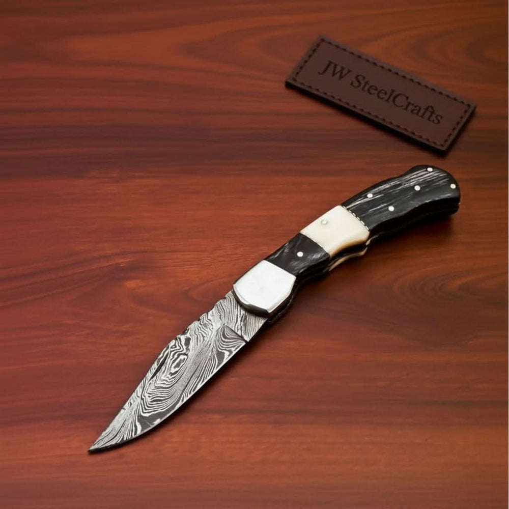     Oaktrail custom Damascus knife with ebony scales and pointed steel blade photographed indoors